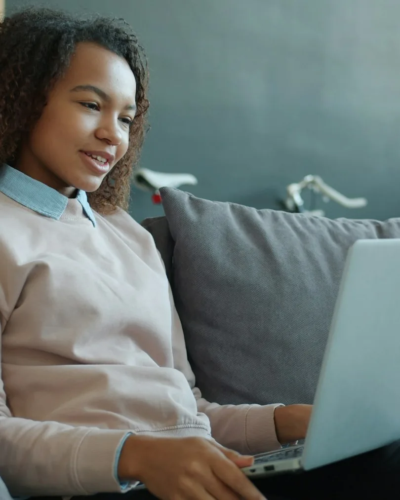 A young woman smiling at her laptop on the sofa at home